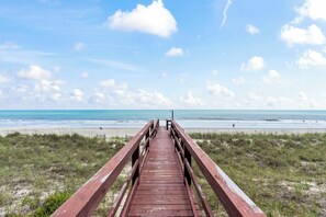 Een houten looppad dat naar een strand leidt, met een heldere lucht.