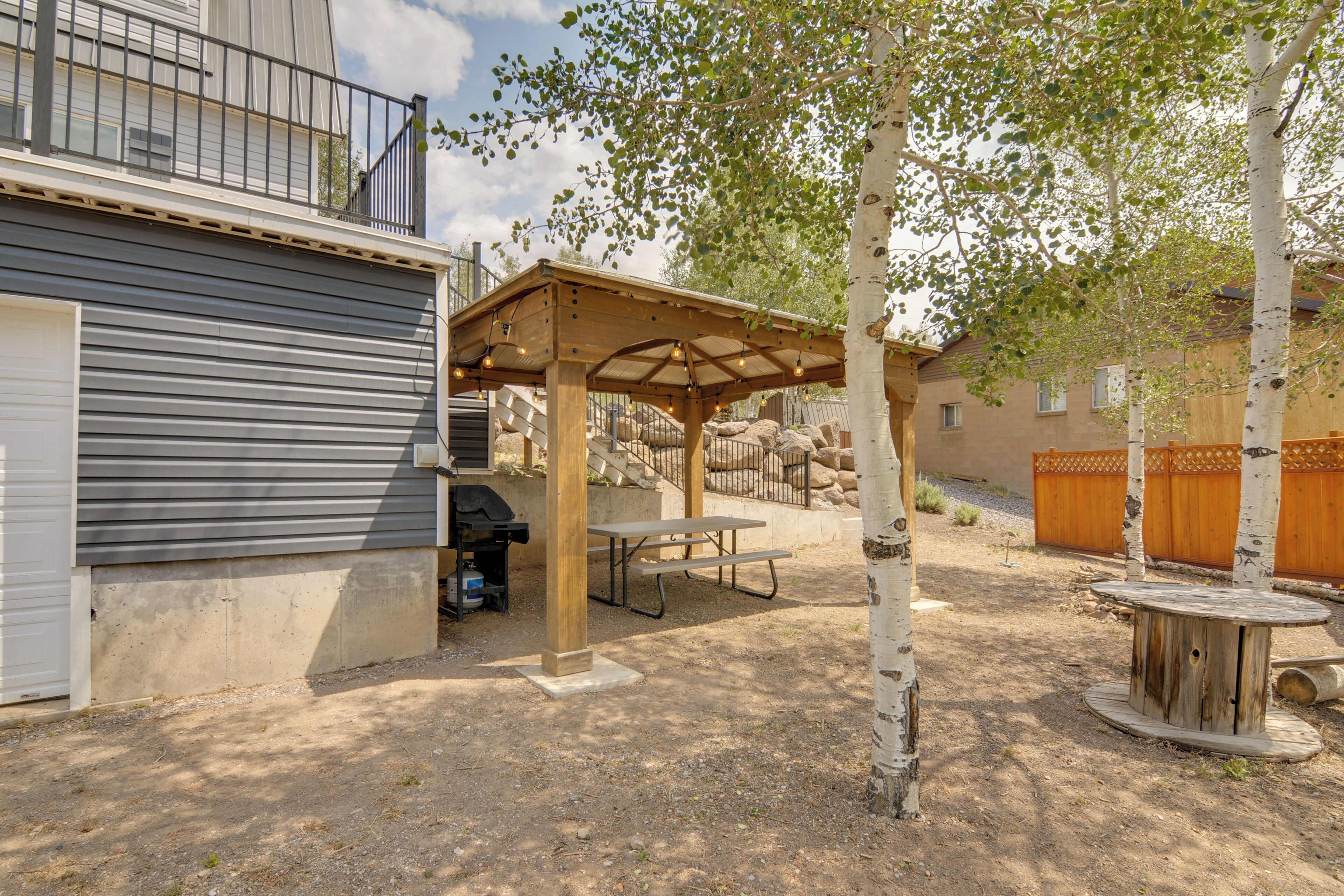 Ein überdachter Patio-Bereich mit Grill, Picknicktisch und Holzmöbeln.