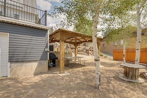 A covered patio area with a barbecue grill, picnic table, and wooden seating.