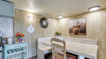 A dining area with a wooden bench, a wall clock, a framed picture, and a small table with a vase of flowers.