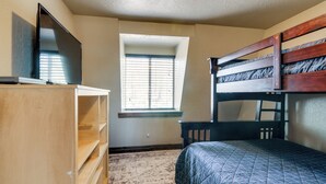 Um quarto com uma cama beliche, uma televisão sobre uma cômoda de madeira e uma janela com persianas.
