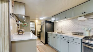 Cozinha com armários azul claro, bancada branca, geladeira de aço inoxidável e painel de azulejos.