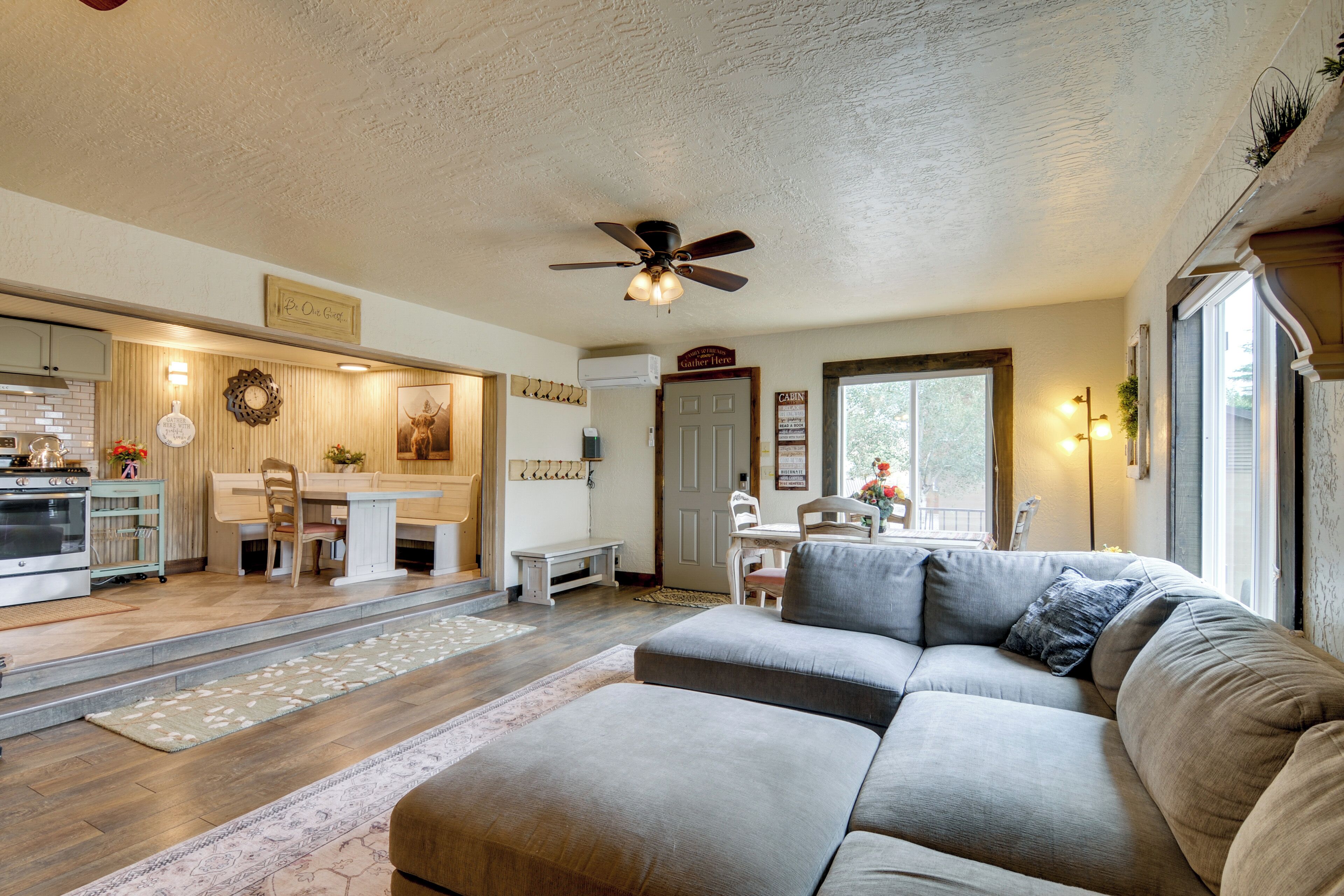 A spacious living area with a large sectional sofa, a ceiling fan, and a kitchen in the background.