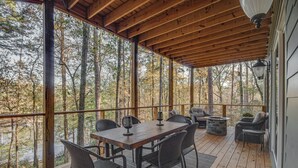 A covered deck with a wooden table and chairs, surrounded by tall trees.