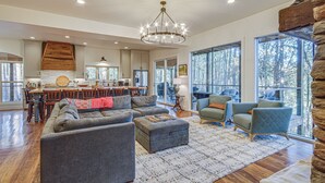 A spacious living area with a large sofa, ottoman, and two armchairs. A dining area with a wooden table and chairs is visible in the background.