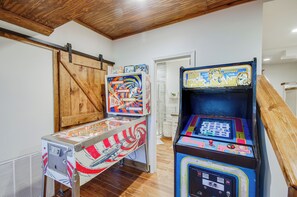 Une pièce avec deux bornes d’arcade, un plancher en bois, une porte coulissante de style grange et une porte blanche.