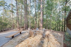 A stone patio with Adirondack chairs and a wooden bench in a forest setting.