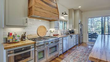 A modern kitchen with stainless steel appliances, wooden accents, and a large window offering a view of the outdoors.