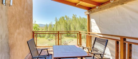 A wooden deck with a table and chairs, a view of trees and mountains, and a covered area with a wooden ceiling.