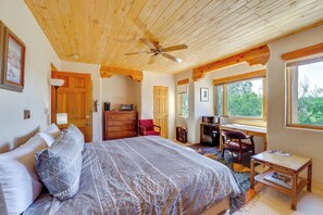 A bedroom with a large bed, wooden ceiling, a desk, and a window with a view of trees. - Des Montes Retreat: Hike, Ski, Swim & Shop! (El Prado)