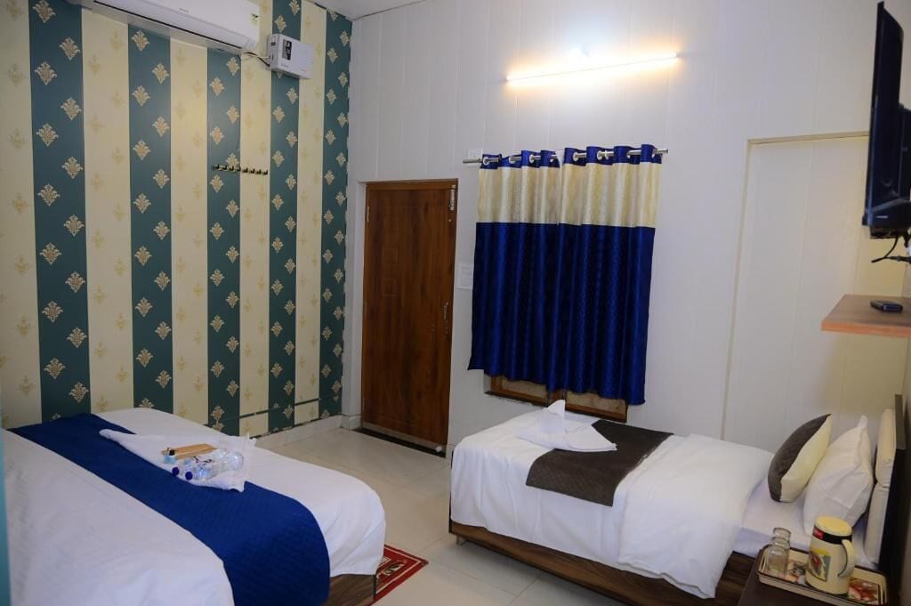 Habitación de hotel con dos camas, una puerta de madera, un televisor y una pequeña mesa con una taza y un tarro.