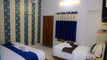 Habitación de hotel con dos camas, una puerta de madera, un televisor y una pequeña mesa con una taza y un tarro.