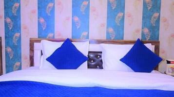 Una cama con ropa de cama azul, almohadas y cabecera azul. Hay dos botellas y un par de pantuflas sobre la cama.