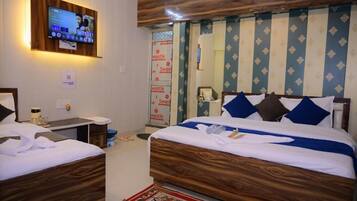 A hotel room with two wooden beds, a television mounted on the wall, and a patterned curtain.
