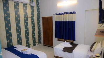 A hotel room with two beds, a wooden door, a curtain, a TV, and a small table with a cup.