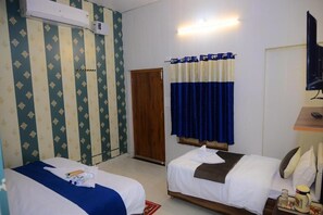 A hotel room with two beds, a wooden door, a curtain, a TV, and a small table with a cup.
