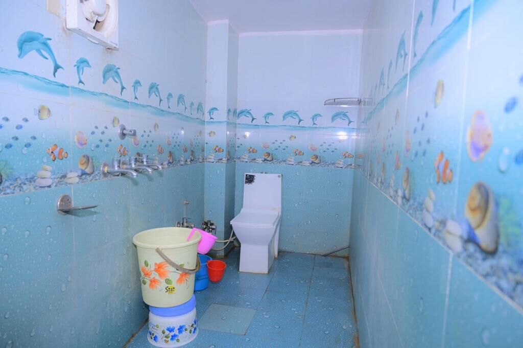 A bathroom with dolphin-themed tiles, a toilet, and a bucket.