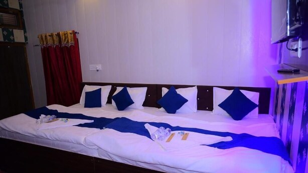 A hotel room with a bed, white linens, blue pillows, and a red curtain. - Siya Ram Guest House (Ayodhya)