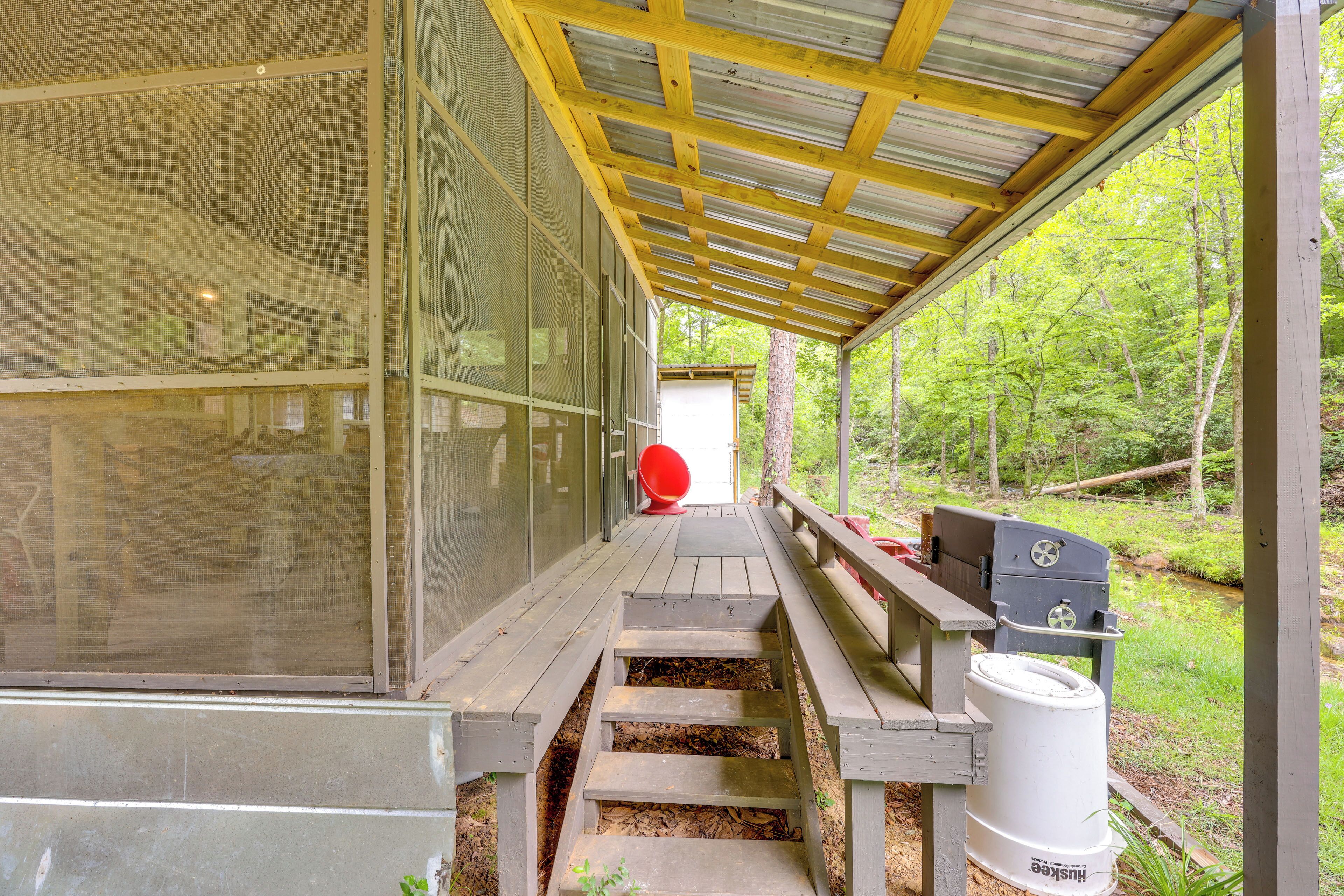 A covered outdoor area with a wooden bench, a grill, and a large window overlooking a forested area.