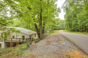 A house with a gravel driveway, surrounded by trees and a road.