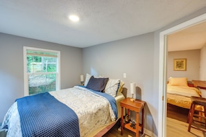 A bedroom with a bed, bedside table, lamp, and a window with a view of greenery.