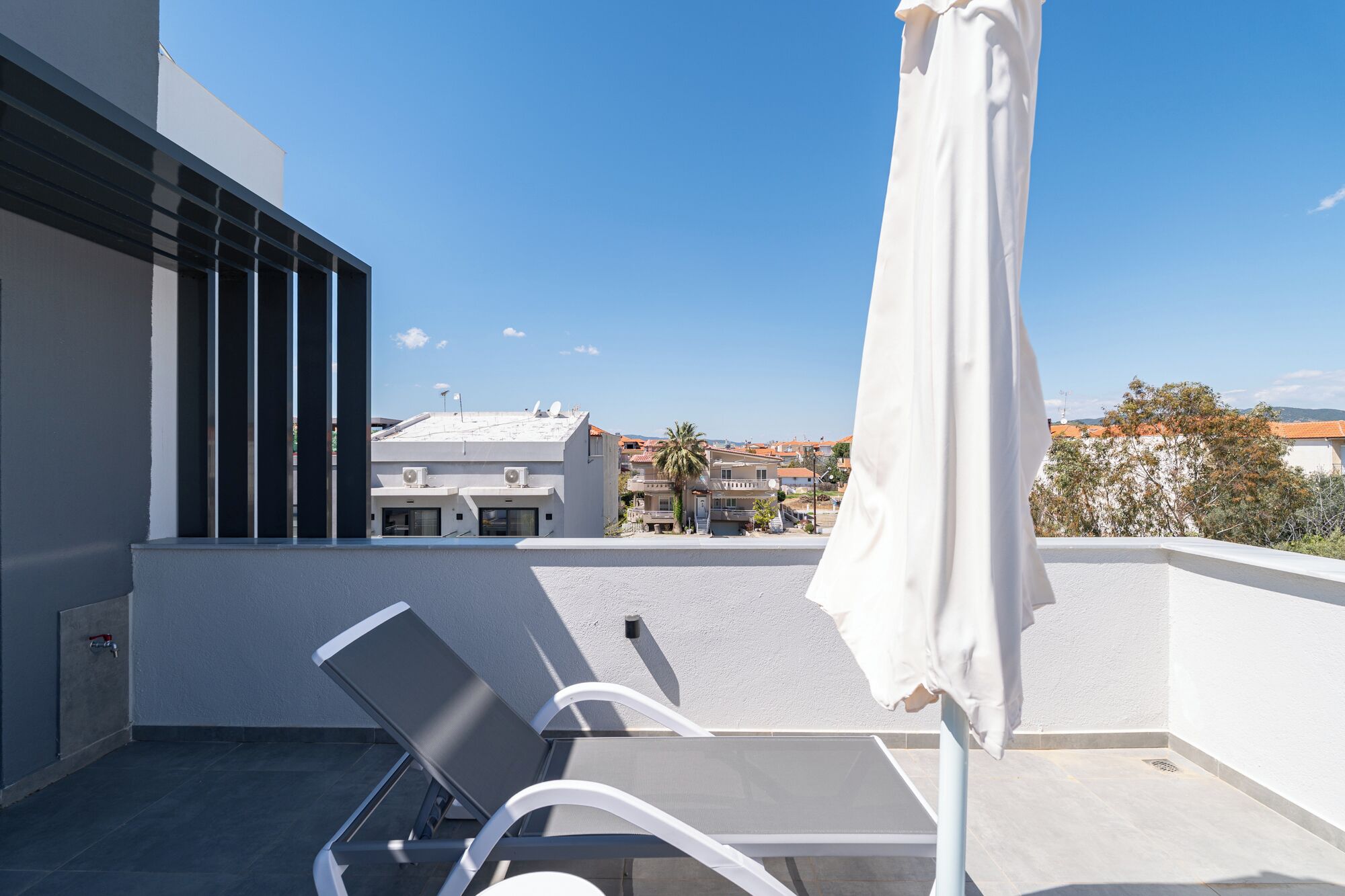 A balcony with a white umbrella, a table, and two chairs.