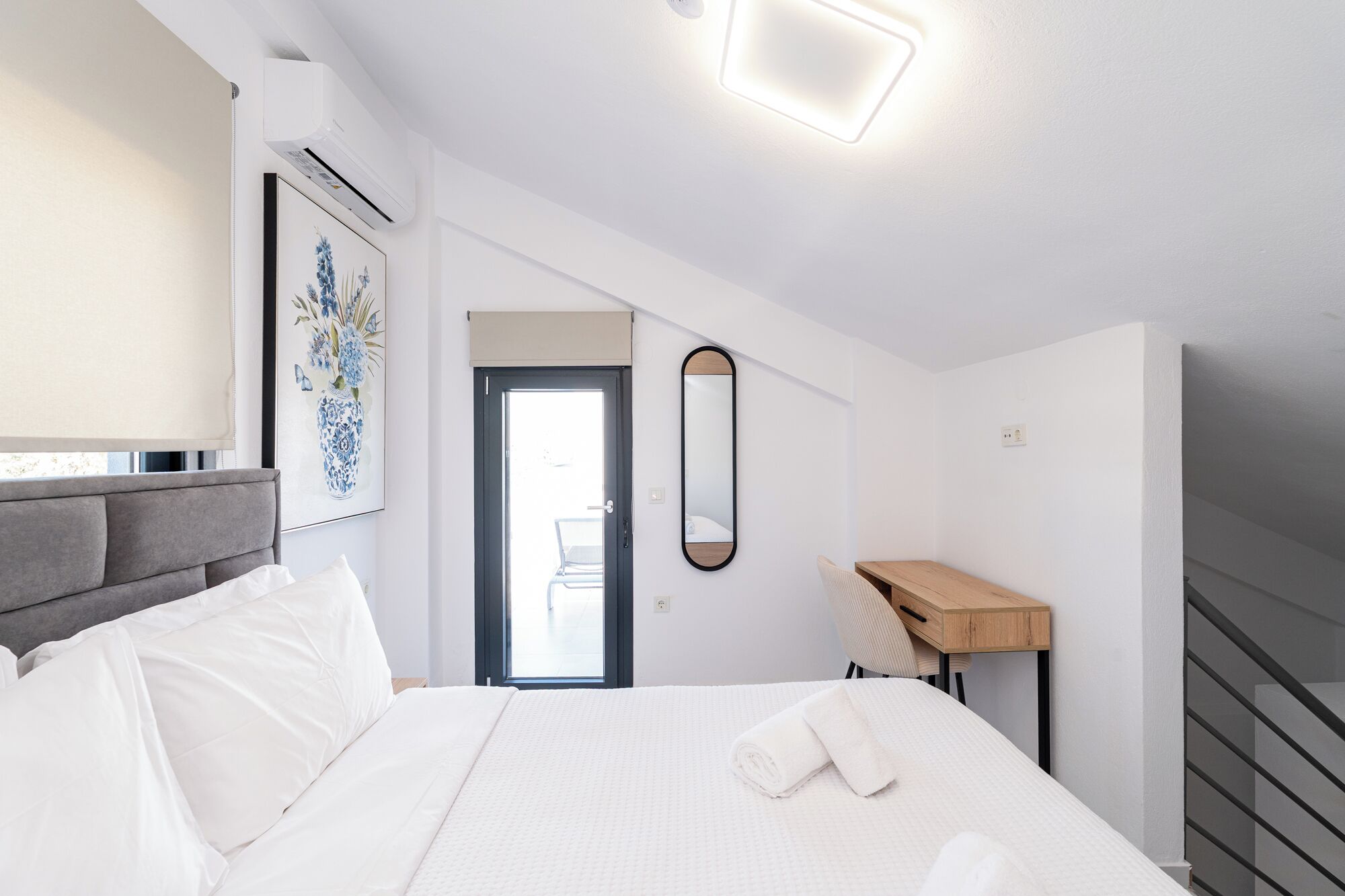 Et moderne hotelværelse med seng, skrivebord, spejl og en dør til en balkon.