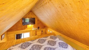 En träinredd interiör med en säng, en tv som är monterad på väggen och ett fönster.