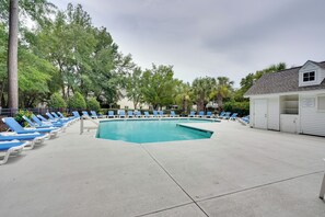 A swimming pool with lounge chairs, a small building with a sign, and trees in the background. - Charleston Townhome Near Credit One Stadium (Charleston)