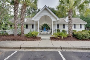 A two-story building with a central arched entrance, surrounded by palm trees and a well-maintained lawn. - Charleston Townhome Near Credit One Stadium (Charleston)