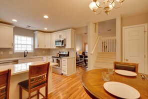 A kitchen with white cabinets, a microwave, and a dining area with a wooden table and chairs. - Charleston Townhome Near Credit One Stadium (Charleston)