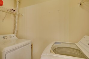 Une buanderie équipée d’un lave-linge et d’un sèche-linge à chargement frontal, d’une étagère en métal sur laquelle se trouve un objet rouge, et d’un mur blanc.