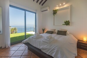 A bedroom with a large bed, a sliding glass door leading to a balcony, and a wall-mounted air conditioner. - Costa Bela Retreat in the Azores: The Perfect Vacation Combining Comfort, Nature, and Tranquility. (Açores)