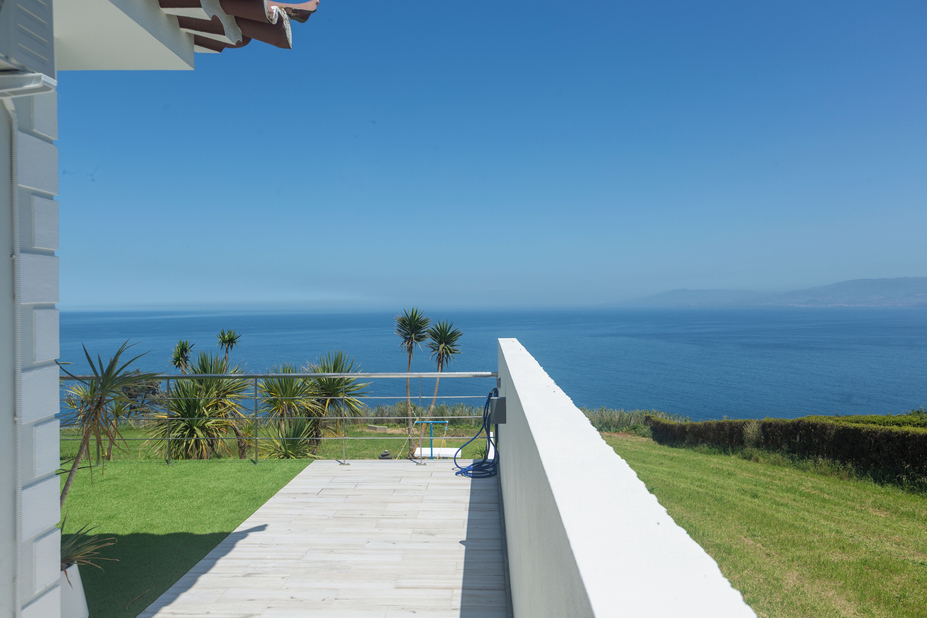 A balcony with a view of the ocean, a white railing, and some greenery.
