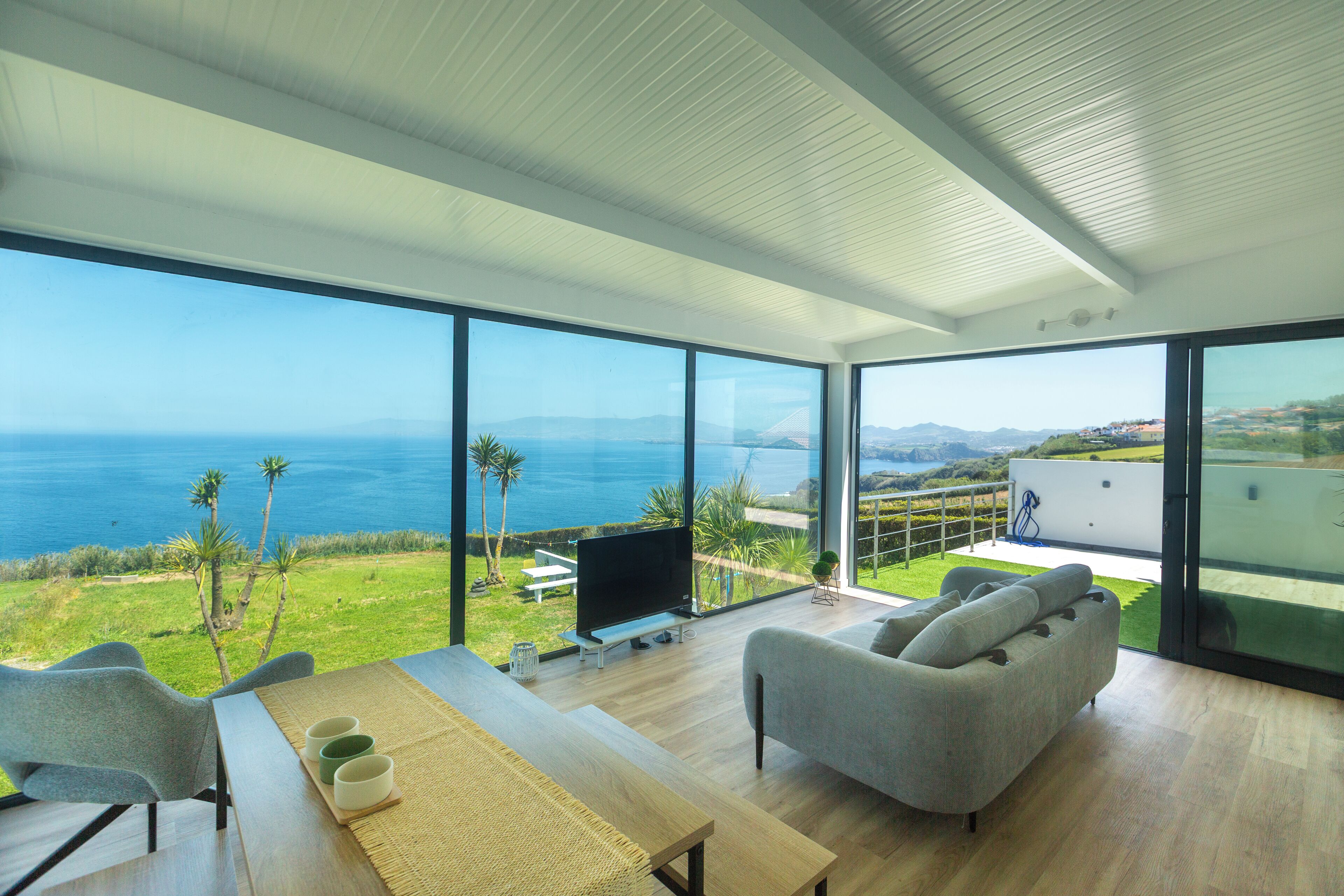 A modern living room with a large glass wall, a sofa, a TV, and a dining table.