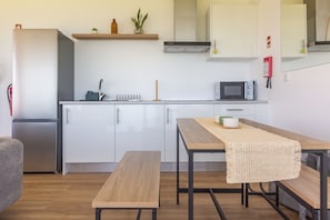 A compact kitchen with a refrigerator, microwave, and a small dining table with a bench. - Costa Bela Retreat Azores: The perfect getaway, offering comfort, nature, and serenity. (Açores)