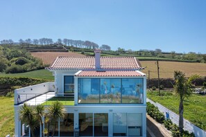 A modern house with a tiled roof, large glass windows, and a green roof. - Costa Bela Retreat Azores: The perfect getaway, offering comfort, nature, and serenity. (Açores)