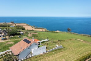A coastal property with a house featuring a tiled roof, a fenced yard, and a view of the sea. - Costa Bela Retreat Azores: The perfect getaway, offering comfort, nature, and serenity. (Açores)