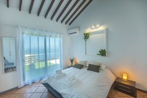 A bedroom with a bed, a bedside table with a lamp, a window with curtains, an air conditioning unit, and a view of the outdoors. - Costa Bela Retreat Azores: The perfect getaway, offering comfort, nature, and serenity. (Açores)