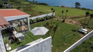 A modern house with a patio area overlooking a grassy landscape and the sea. - Costa Bela Retreat Azores: The perfect getaway, offering comfort, nature, and serenity. (Açores)