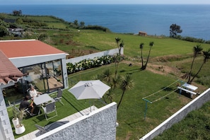 A modern house with a patio area overlooking a grassy landscape and the sea. - Costa Bela Retreat Azores: The perfect getaway, offering comfort, nature, and serenity. (Açores)
