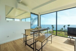 A modern room with a large window, a wooden table, a bench, and a flat-screen TV. - Costa Bela Retreat in the Azores: The Perfect Vacation Combining Comfort, Nature, and Tranquility. (Açores)
