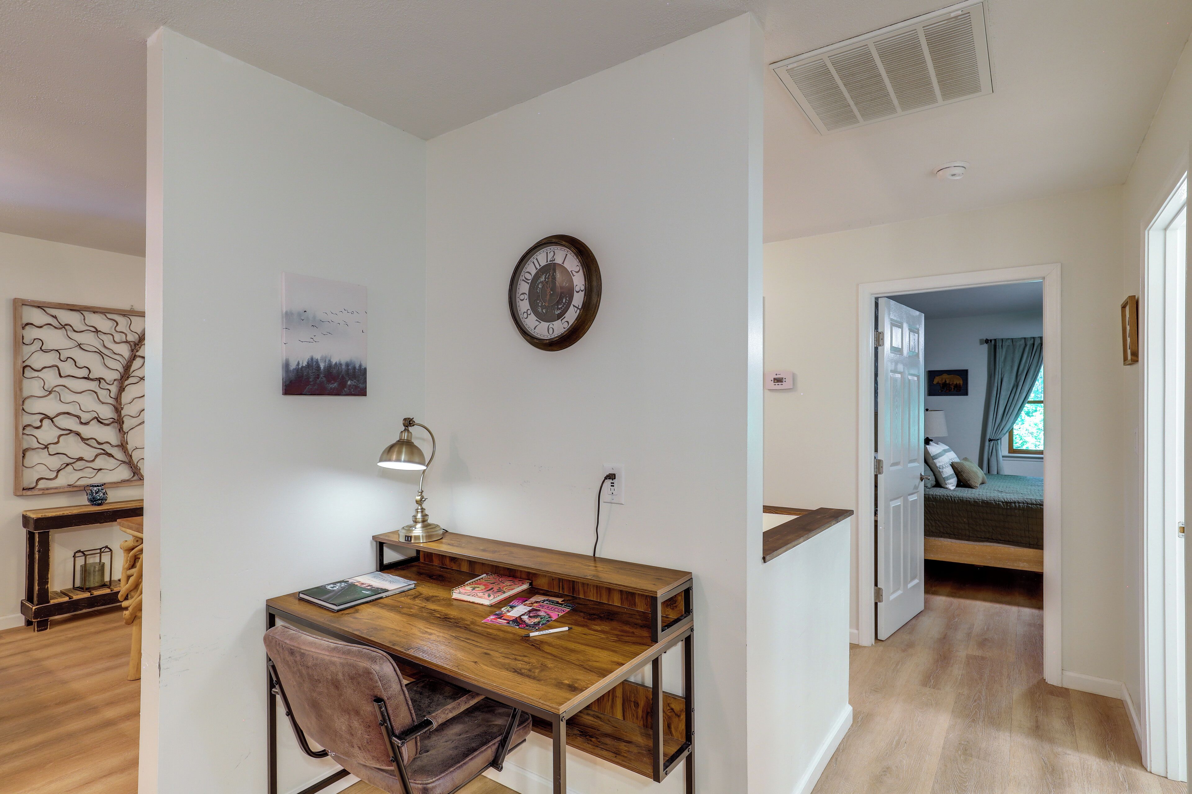 Een kamer met een houten bureau, een stoel, een wandklok, een bed en een deur naar een andere kamer.