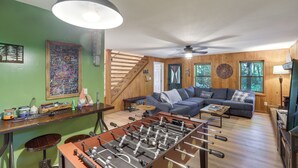 A cozy living room with a sectional sofa, a foosball table, and a staircase leading to an upper level. - Mins from AVL, Woodsy Weaverville Retreat (Weaverville)