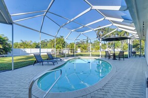 A covered outdoor swimming pool with lounge chairs and tables, surrounded by a white metal frame and a clear blue sky. - Modern 2-Unit Combo w/ Pool: 'Naples Hideaway' (Naples)