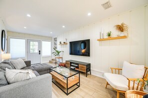 A modern living room with a grey sofa, a glass coffee table, a wooden side table, a black entertainment unit, and a wooden chair. - Modern 2-Unit Combo w/ Pool: 'Naples Hideaway' (Naples)