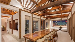 Um quarto espaçoso com uma longa mesa de jantar de madeira, várias cadeiras e teto alto com vigas aparentes.