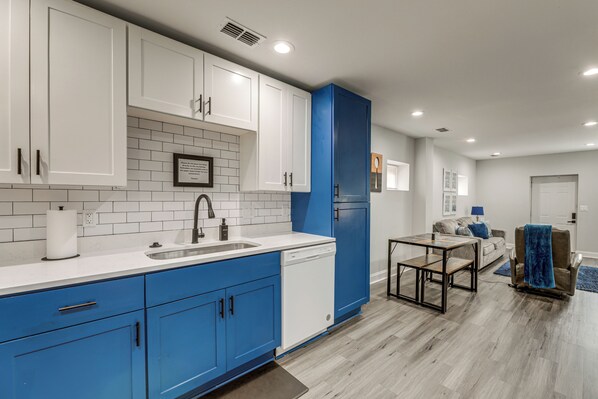 A modern kitchen with white and blue cabinets, a dishwasher, and a dining area with a table and chairs. - 5 Mi to Nissan Stadium & Broadway! (Nashville)