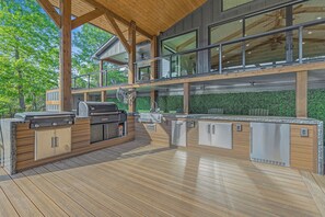 Eine großzügige Außenküche mit Grill, integrierten Geräten und einer Holzterrasse.