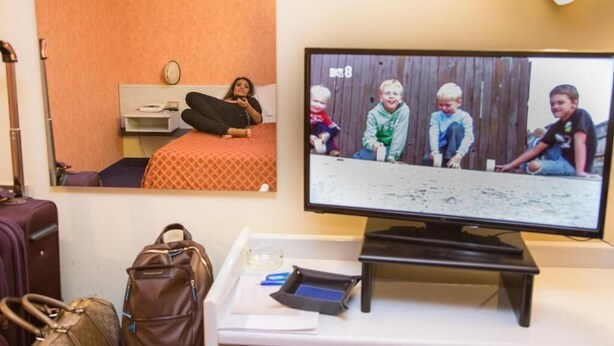 A hotel room with a bed, a television, a desk with a laptop, a handbag, and a suitcase.
